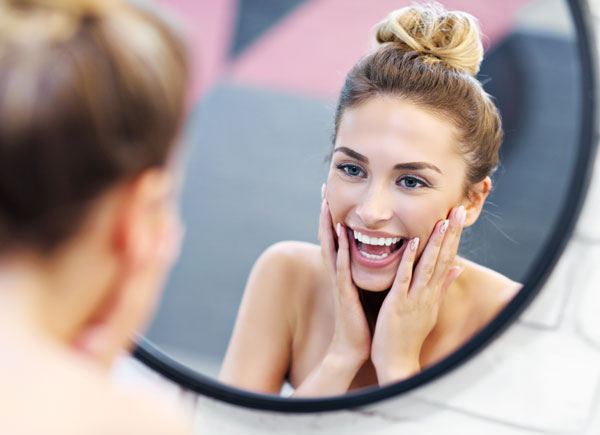 Young woman smiling at mirror after whitening her teeth with Aspen Orthodontics teeth whitening treatment
